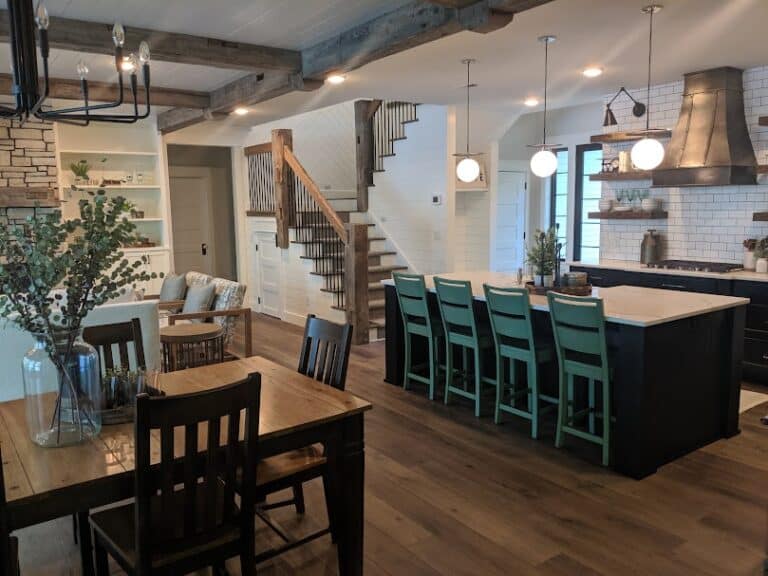 Open-concept kitchen and dining area featuring wide-plank rustic flooring, exposed wooden ceiling beams, and a large island with teal barstools.
