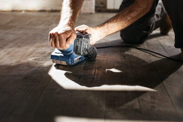 Men's hands make repairs at home. Grinding machine with a wooden floor; oak floor restoration