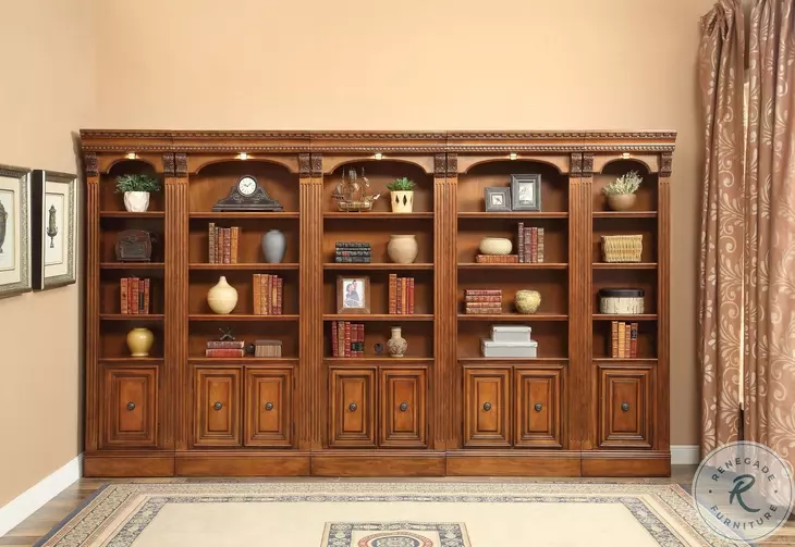 A large, ornate reclaimed wood bookcase with shelves filled with books, vases, and decorative items. The bookcase has cabinets at the bottom and is set against a beige wall with framed art and brown curtains on either side.