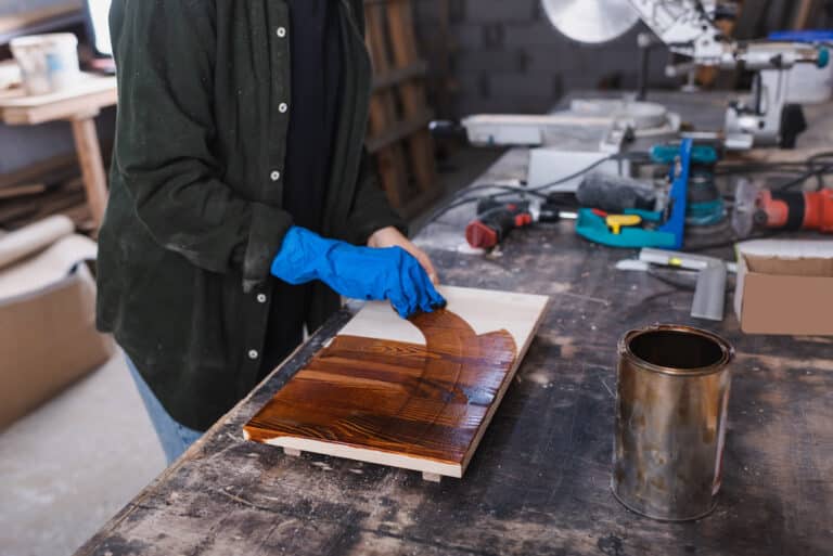 person in rubber glove applying wood stain on rustic picture frame