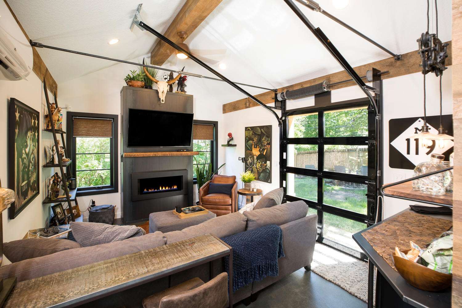 a look at all the features in the Minnetonka man cave, such as the window panels in the garage door, the ceiling beams, and the tv viewing area with the couch and reclaimed wood mantel