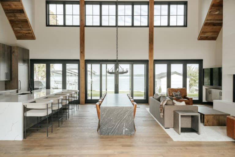 Modern lodge living area with lots of natural light through full length windows. Decorative reclaimed wood box beams reach from floor to ceiling. A modern quarts dinner table crosses the room.