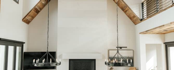 Modern lodge with reclaimed wood ceiling paneling and reclaimed wood box beams. Contemporary table and kitchen island cross the room. A modern, white fireplace dominates the back wall.