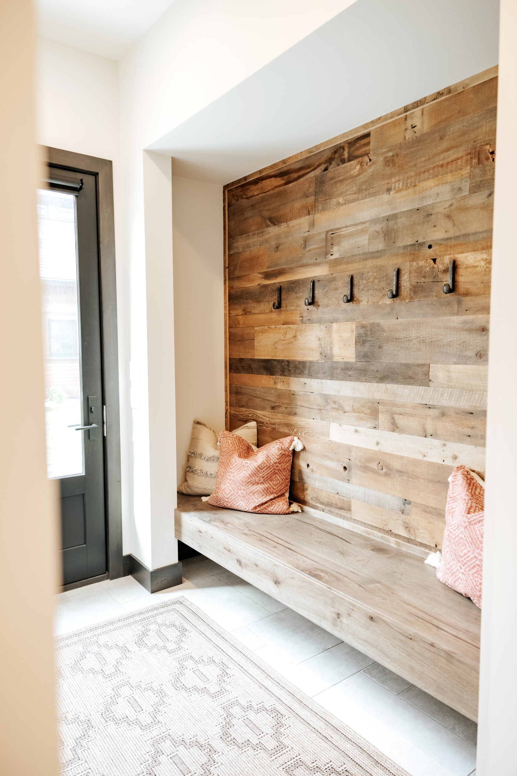 Reclaimed wood paneling accent wall in a mudroom with wrought iron coat hooks.