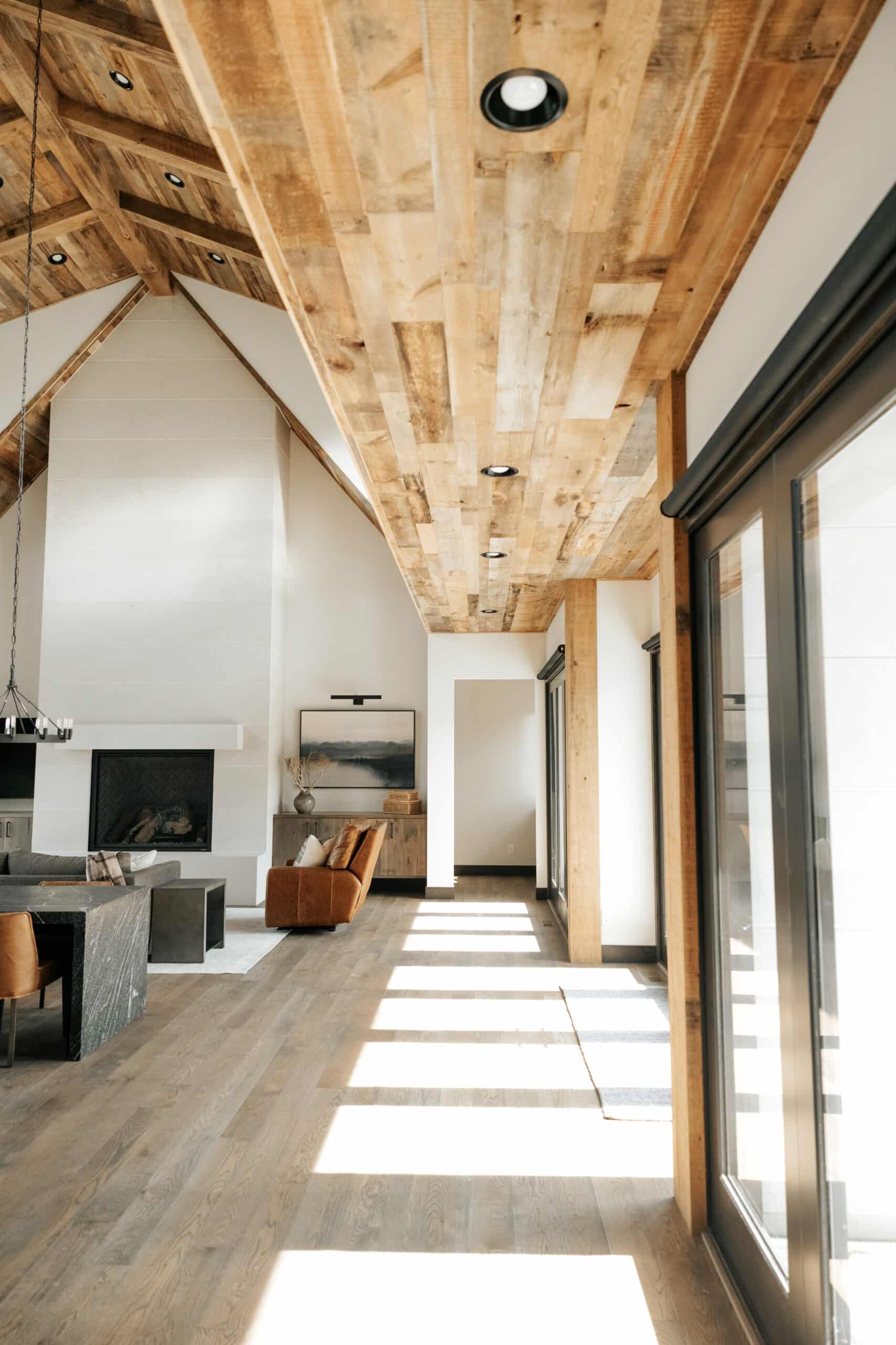 A modern lodge grand hall looking underneath a balcony with reclaimed wood paneling on the ceilings. Lots of natural light reflects off of white walls and modern design.