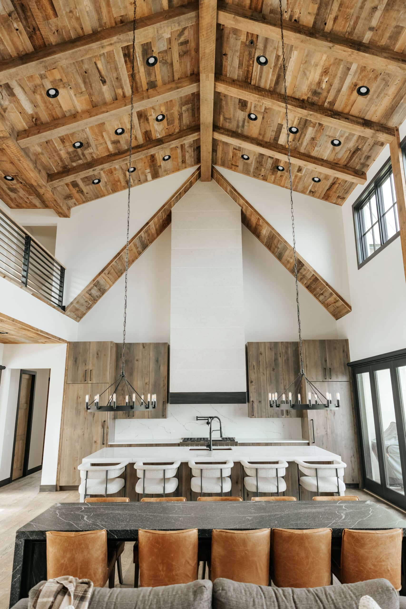 Modern lodge grand hall and kitchen with reclaimed wood panel vaulted ceilings with recessed lights. Reclaimed wood box beams decorate the ceiling.