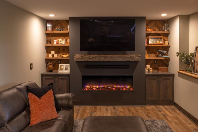 A hand-hewn reclaimed wood mantel floating above a wide electric fireplace. Reclaimed wood wall paneling and shelves decorate the walls on either side.