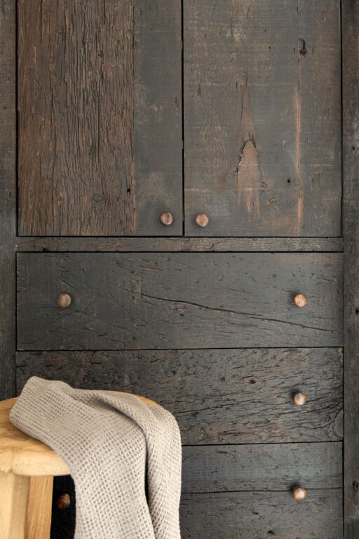 A close up of custom reclaimed wood cabinets made from dark stained antique pine wood. Deep marks and wood grain is visible in the cabinet doors and drawers.