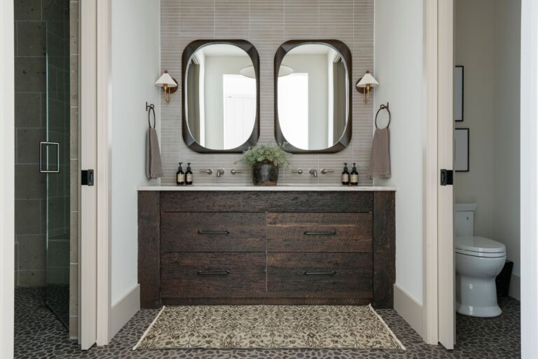 Custom reclaimed wood vanity in a guest bathroom. The vanity has double sinks and is made in a dark stained antique pine. A walk in shower is visible to one side and a toilet to the other.