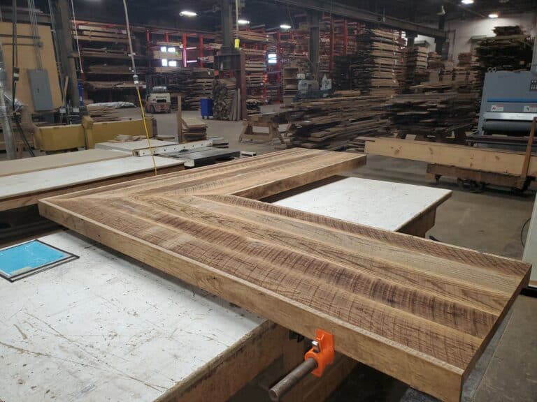 Reclaimed wood bar top being clamped together in a wood workshop with shelves of timbers in the background.