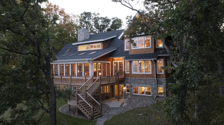 Cottage style luxury home on Pelican lake, Minnesota. Custom home built by Nor-Son Custom Builders. Surrounded by trees, the home has wood shingle siding, lower level walk out, and a steep roof with gabled windows.