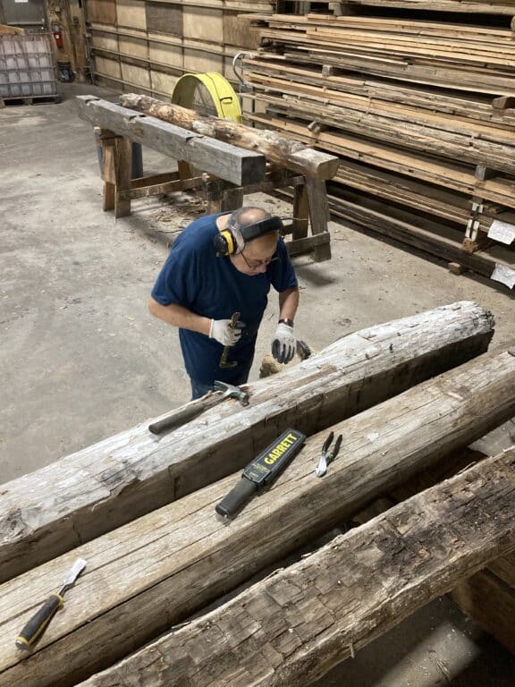 Wood worker reclaiming an old growth wood timber in a warehouse wood workshop.