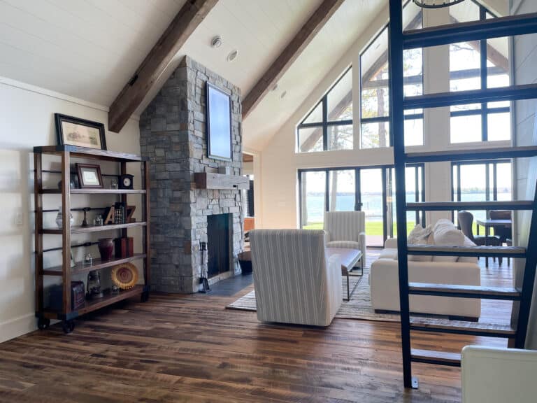 A cozy living room with a stone fireplace and a lot of natural light from floor to ceiling windows. The reclaimed hardwood floors are made from skip planed oak.