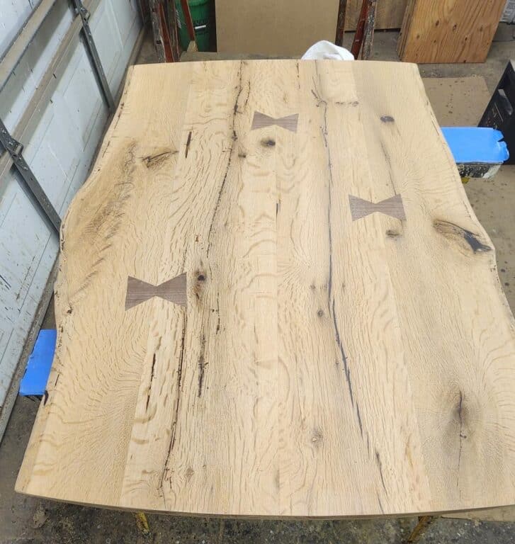 Unfinished reclaimed wood tabletop in a woodshop. The tabletop is irregular shaped with wood ties embedded in it to link the planks together.