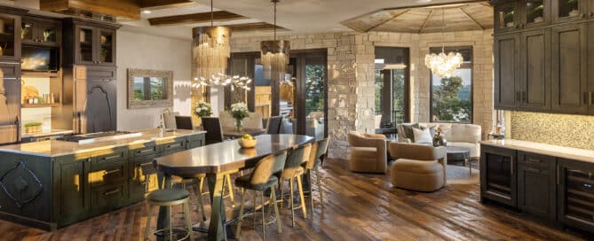 A living room and kitchen area with weathered antique reclaimed hardwood flooring, stone-faced walls, and custom wood cabinetry.