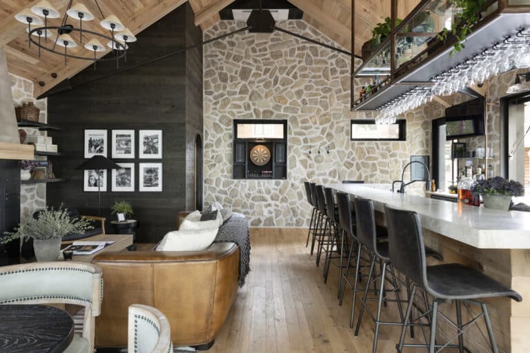 A custom home bar with lots of natural materials. A stone faced wall is at the back end with white oak ceilings and darker wood accents. White oak reclaimed hardwood flooring.