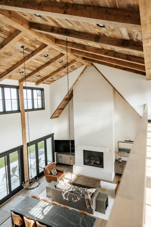 Weathered antique reclaimed wood box beams used as decorative ceiling beams in a grand room with a high vaulted ceiling. The reclaimed wood ceiling beams are placed as rafters with matching reclaimed wood paneling along the ceiling itself. Below is a bright modern design.