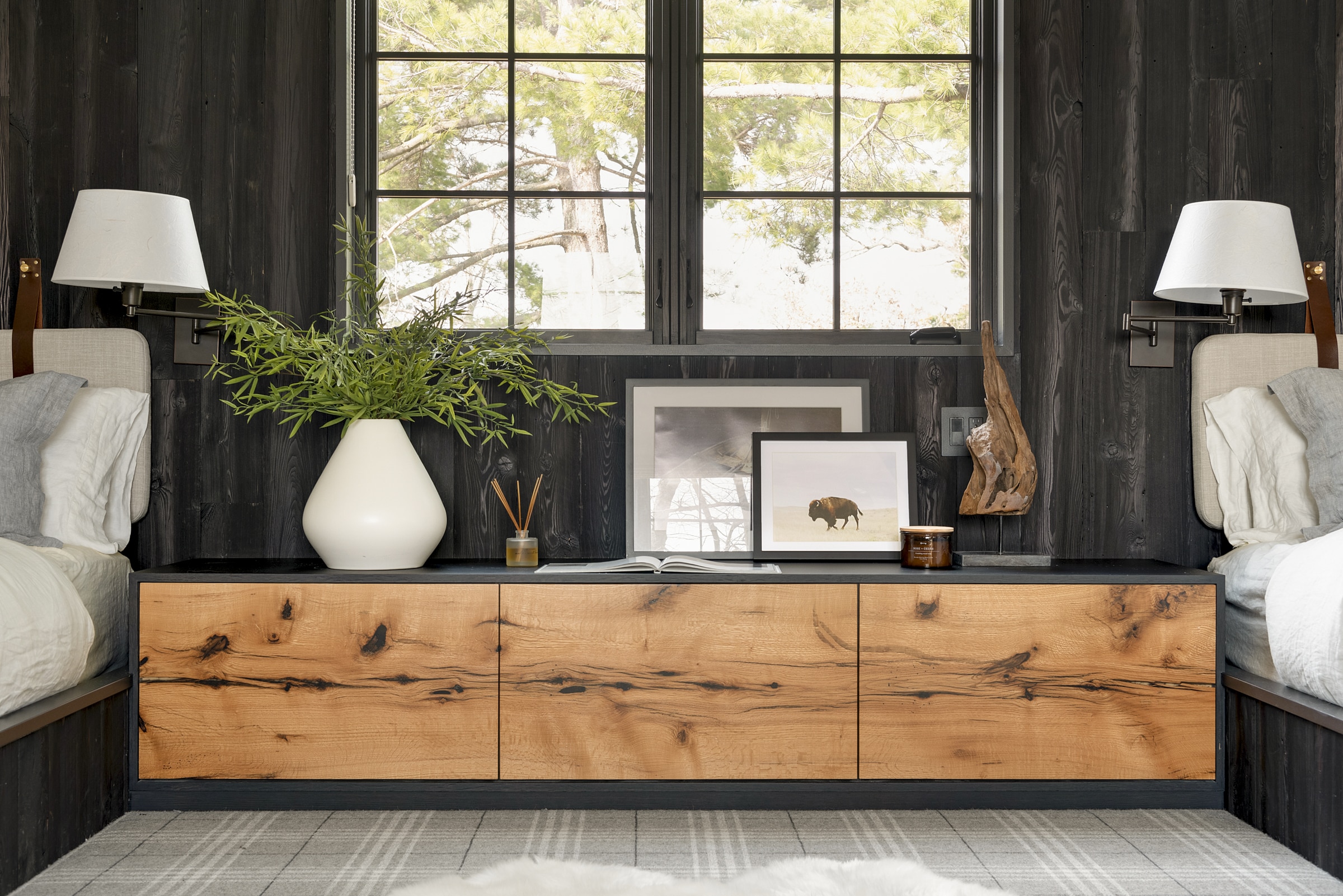 Twin bedroom with Shou Sugi Ban paneling wall between beds and behind a natural wood cabinet.