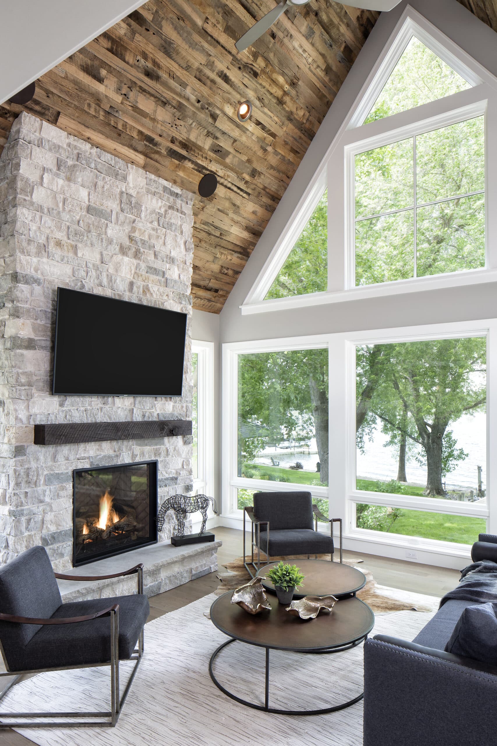 Modern living room with stone fireplace, timber mantel, and vaulted ceiling clad in reclaimed wood paneling