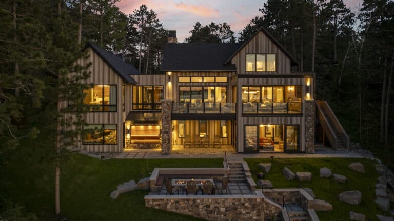 Luxury custom home on a lake at twilight with lit up windows and glowing reclaimed wood siding