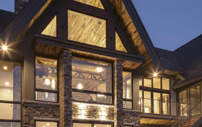 Modern rustic lodge at night with glass walls and reclaimed wood soffits on high gables