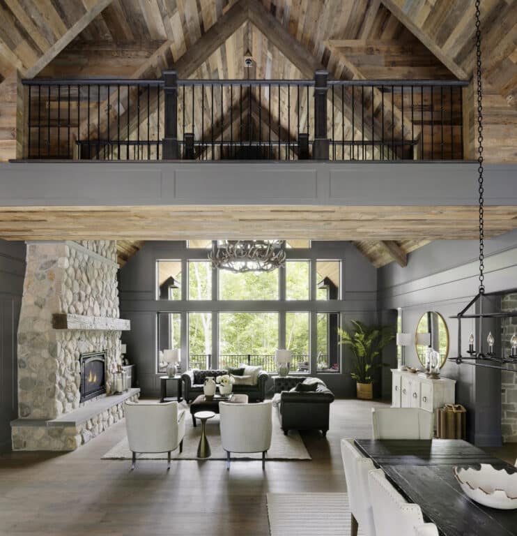 Spacious cozy living room with vaulted reclaimed wood ceiling, stone fireplace, and large windows bringing in natural light; features a mix of modern and rustic cozy interior design elements with soft seating, a chandelier, and warm home vibes.