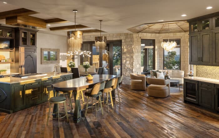 Luxury kitchen and living area with reclaimed wood flooring, stone walls, and elegant chandeliers, blending rustic warmth with modern style for a cozy interior design.