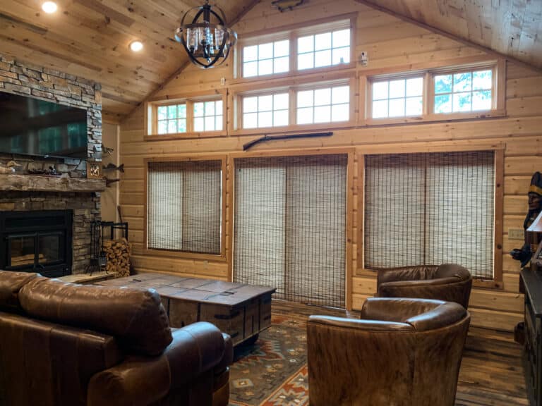 Rustic living room with a reclaimed wood wall and natural wood paneling for walls, featuring a stone fireplace, leather furniture, and a cozy cabin-style atmosphere