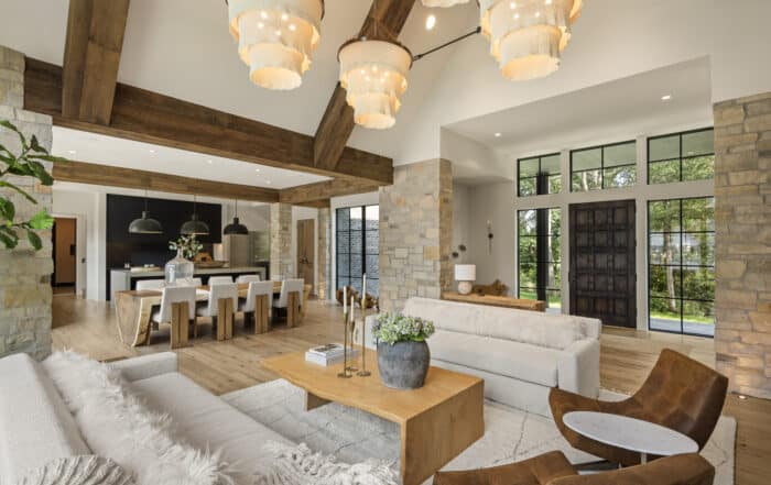 Alt text: A spacious living room and kitchen featuring warm wood beams, stone accents, and modern neutral furnishings, offering elegant traditional interior design with inviting natural textures and open-concept flow