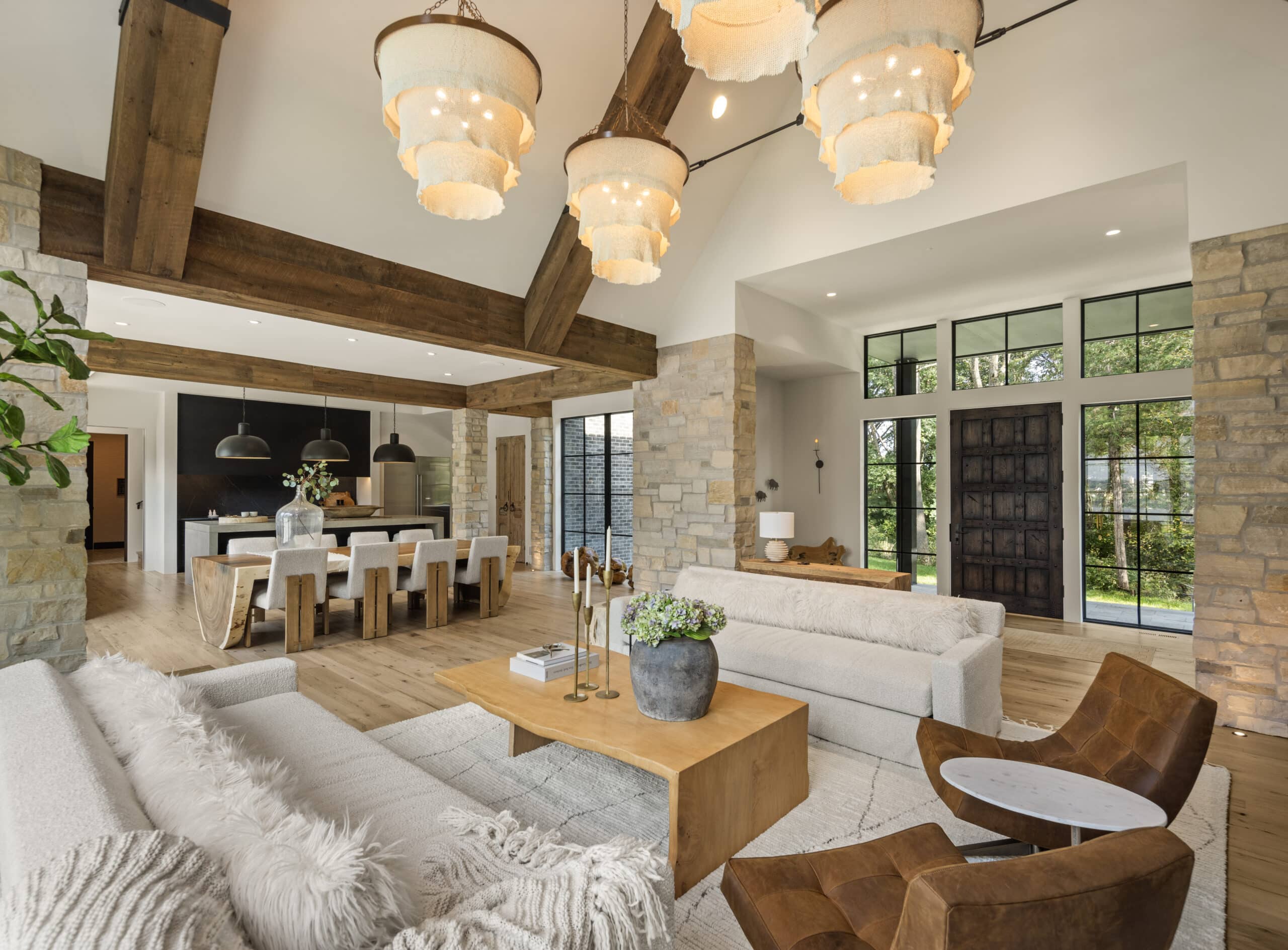 Nor-Son – Lindus Residence (4) Alt text: A spacious living room and kitchen featuring warm wood beams, stone accents, and modern neutral furnishings, offering elegant traditional interior design with inviting natural textures and open-concept flow