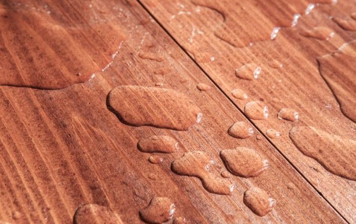 Water droplets sitting on a finished wood surface, showing moisture damage and why it’s important to remove stain from wood properly.